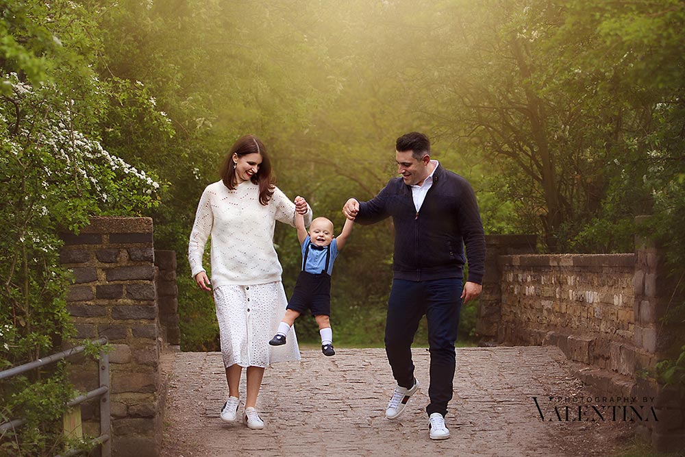 mum and dad are holding and swinging baby during a family photoshoot in London.