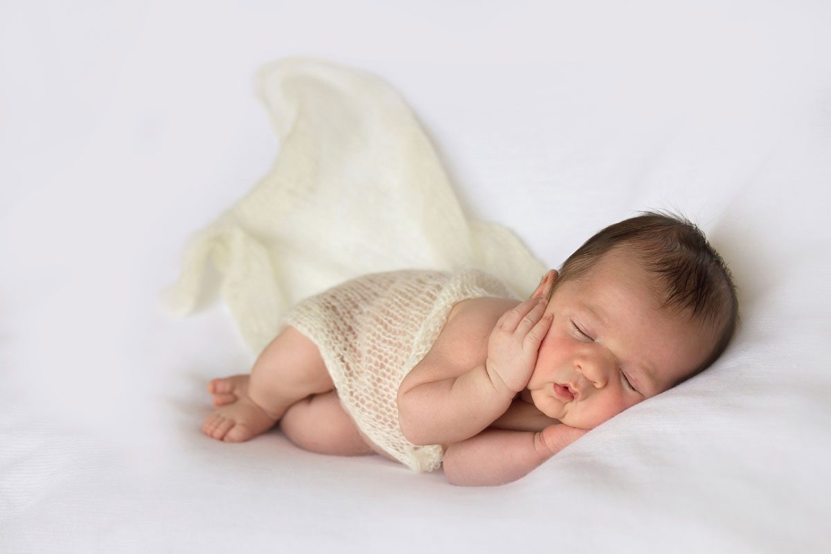 Newborn baby sleeping on a white blanket, wrapped in a light swaddle