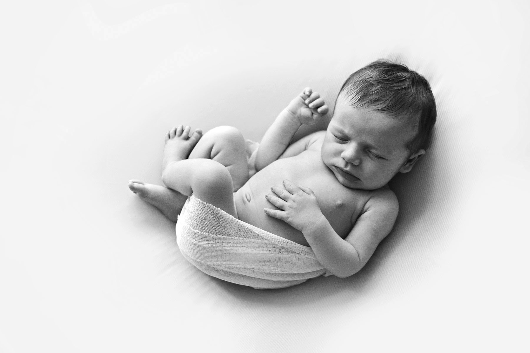 Black and white photo of a newborn baby lying on a soft surface
