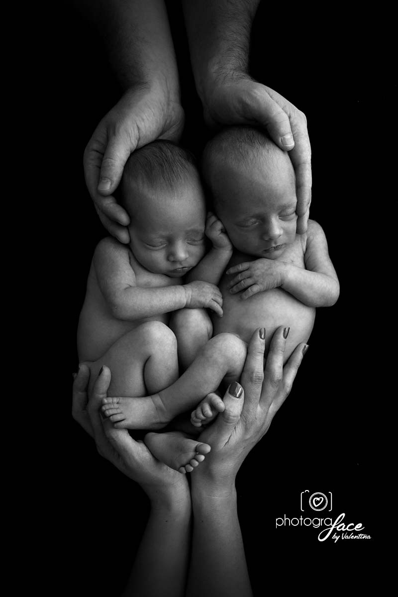 newborn twins on a black background with parents hands