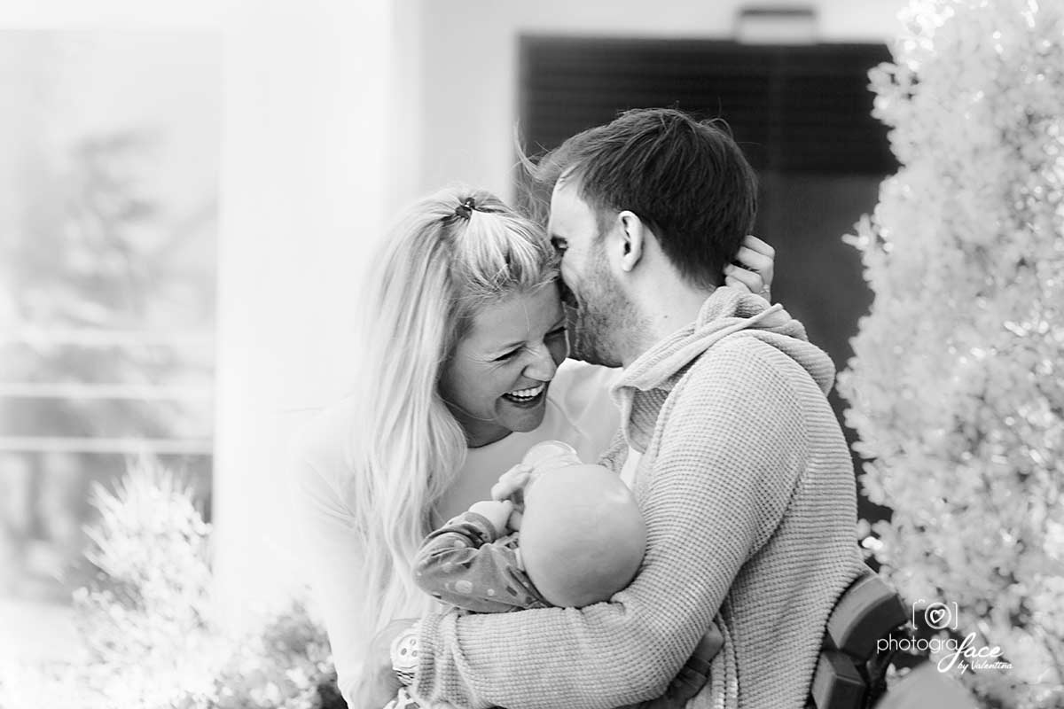 mum and dad hugging and laughing while holding baby - value of photos