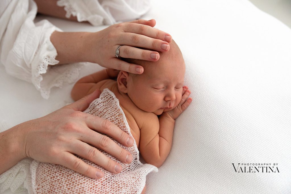 portrait of a newborn sleeping on his tummy. Mum and dad have their hands on his back and head.
