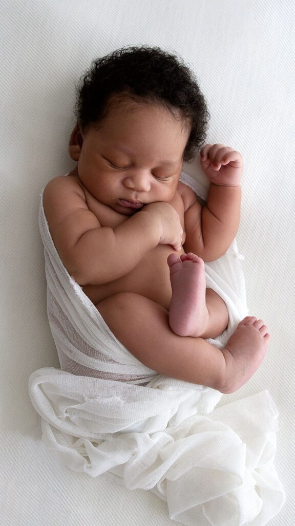 Newborn baby wrapped in soft white fabric, asleep on a light background – simple, timeless newborn photography in London