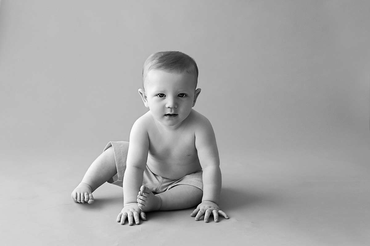 Black and white studio portrait of a baby boy sitting on the floor.