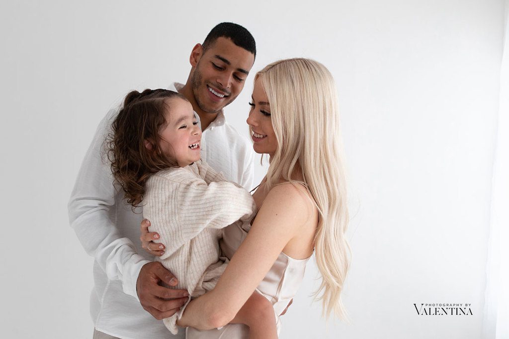 happy moment during a family photoshoot. Mum is holding her daughter and dad is behind them, they all look at each other smiling.