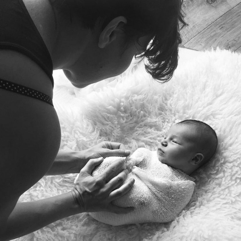 Why Hiring a Professional Newborn Photographer Matters: behind-the-scenes black and white photo of a professional newborn photographer gently wrapping a baby in a soft blanket during a posed newborn session.