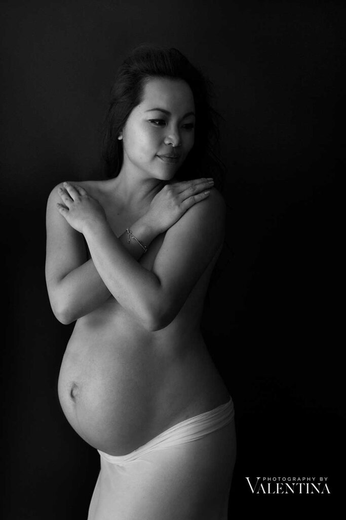 Pregnant woman holding her arms around her chest and looking serene during a London studio maternity shoot.