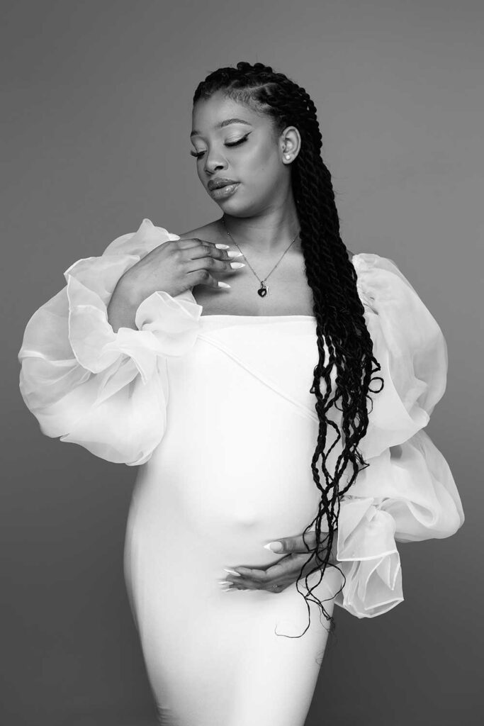 maternity portrait: mum is wearing a white dress and gently posing with hand on the belly
