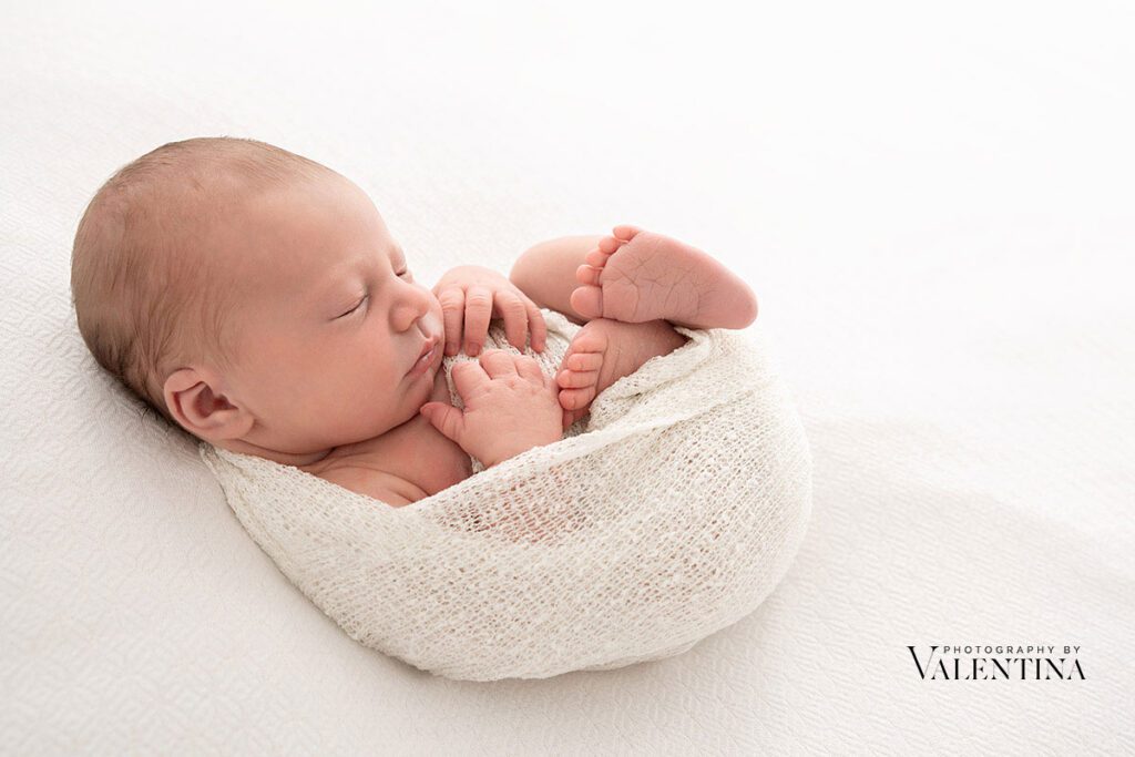 Newborn baby wrapped in a white fabric and snuggled comfortably during a newborn photoshoot in London