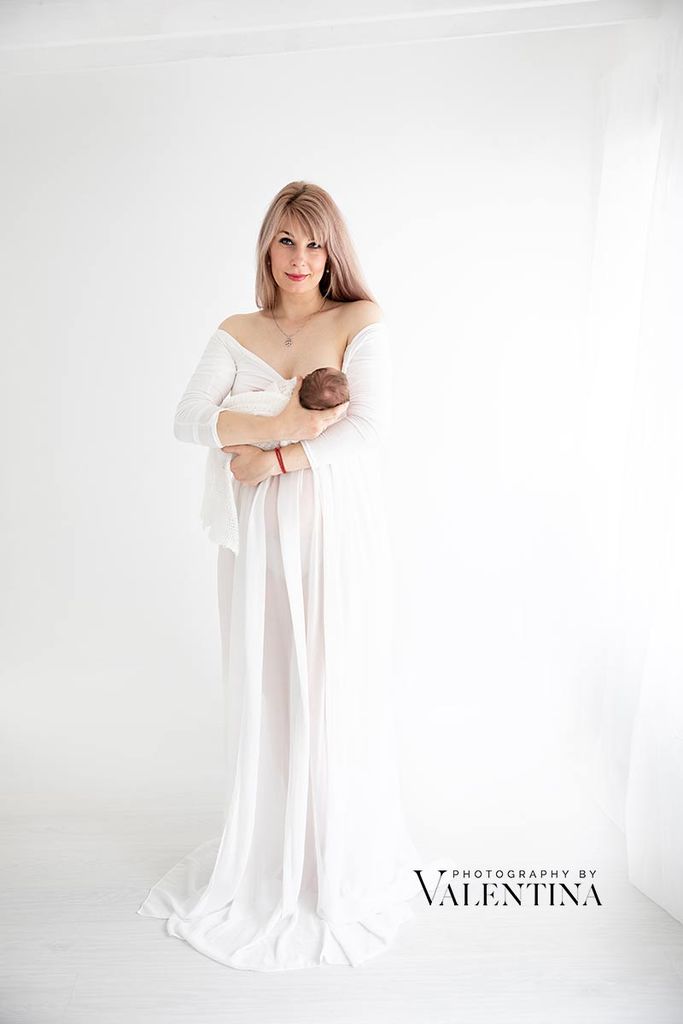 A beautiful newborn and mother portrait during a newborn photography session. The mum is holding her baby in a flowing white gown, while she is breastfeeding.