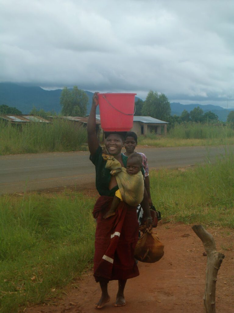 Scene from rural Malawi that inspired the breastfeeding book – mother carrying baby on her back and basket on her head, symbolising strength and community.