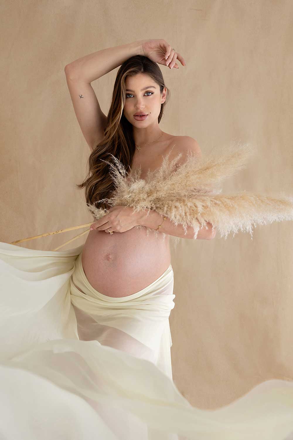 Artistic maternity portrait with pampas grass, highlighting natural tones and grace.