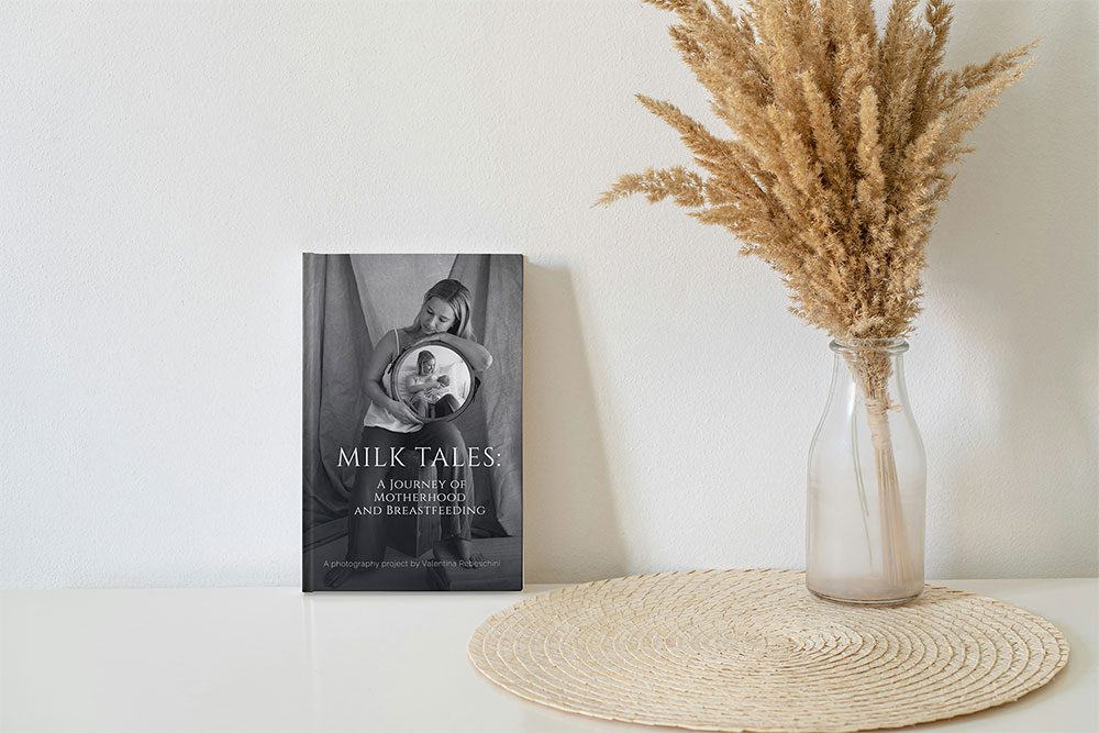 Cover of the breastfeeding book 'Milk Tales: A Journey of Motherhood and Breastfeeding' displayed on a white shelf beside a vase of dried flowers.