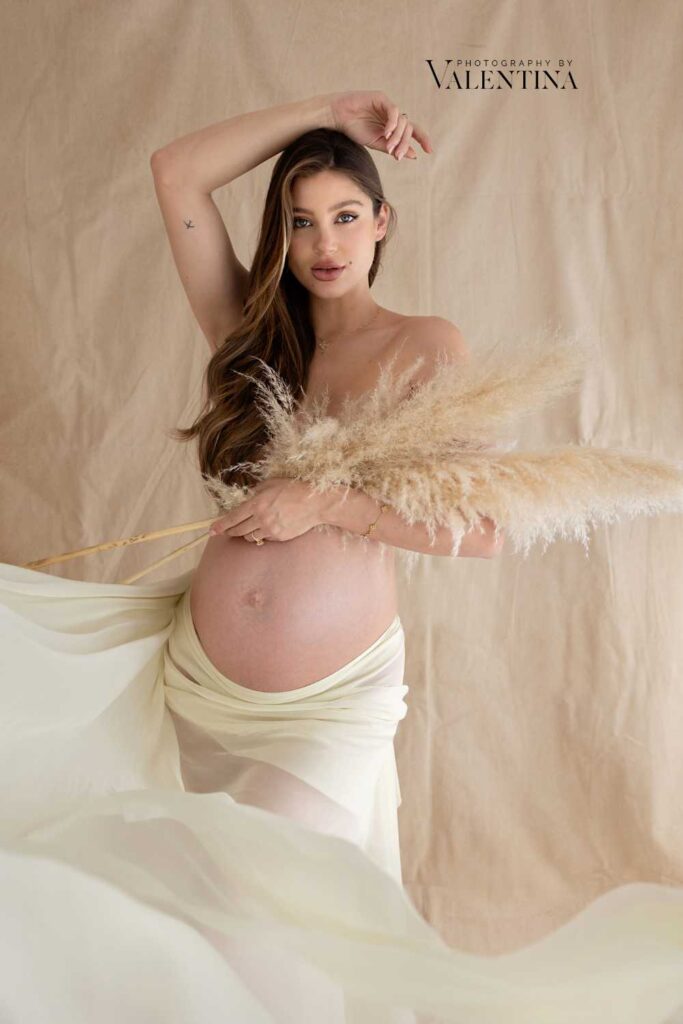 Maternity portrait: mum is holding some pampas on her nude chest and wearing a flowy fabric around her hips. 