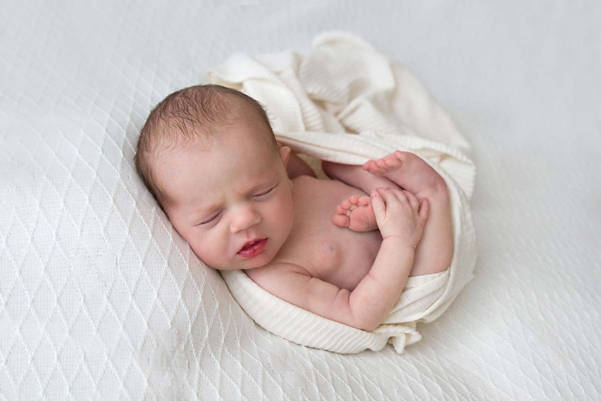 Newborn baby peacefully sleeping in a soft white wrap, minimal and natural photography style.