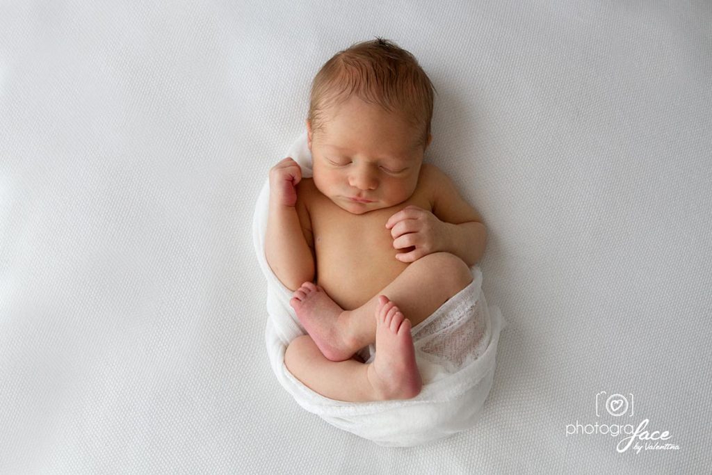 Newborn baby curled up and asleep in a white cloth,