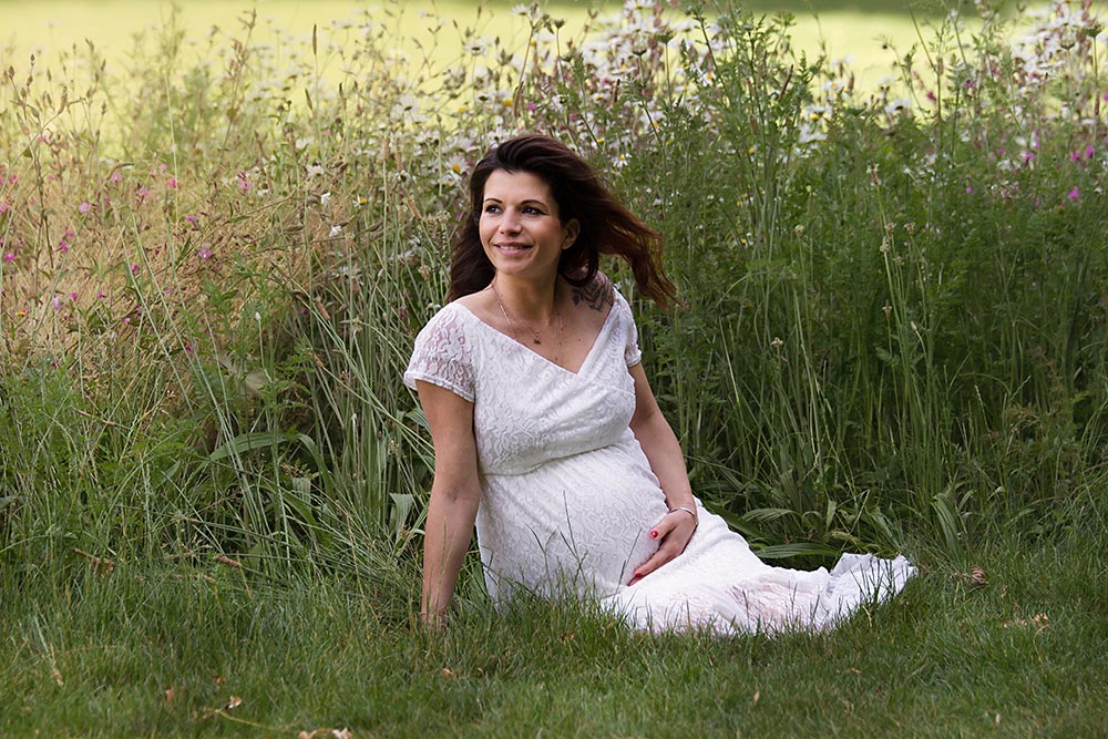 Pregnant woman sitting in a meadow wearing a white dress