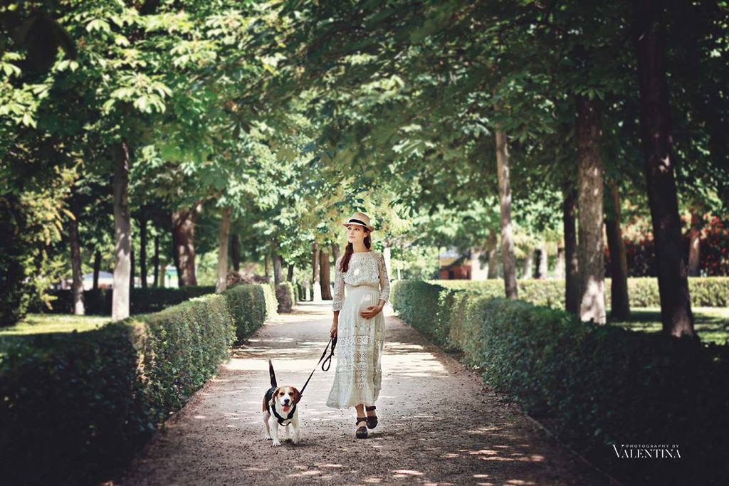 Pregnant woman walking her dog on a park wearing boohoo dress cradling her belly in a relaxed and confident maternity portrait.
