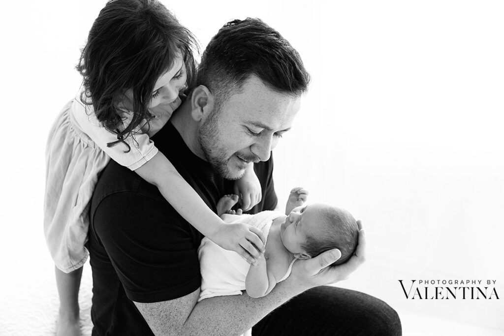 Black and white portrait of dad and his girls during a newborn photoshoot in London. A storytelling image that speaks love and connection.