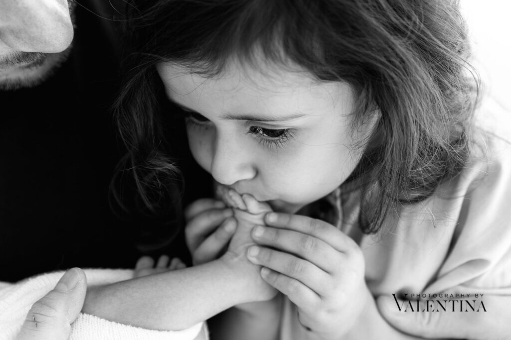 close up of big sister kissing newborn foot. 